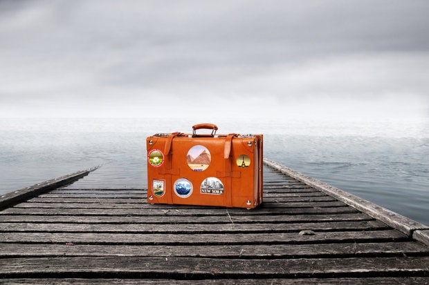 outsourcing suitcase with travel stickers at edge of dock