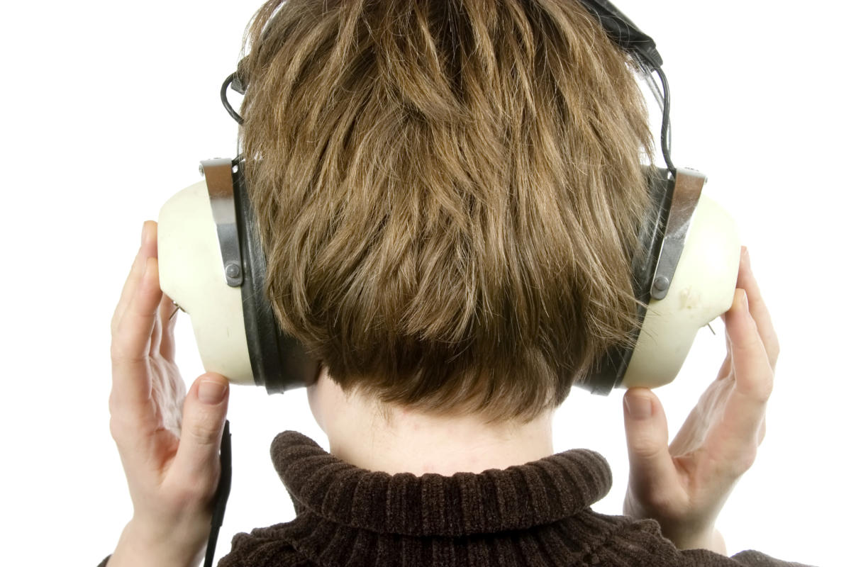 the back of a person head who is listening to music with large retro earphones. their hands are up