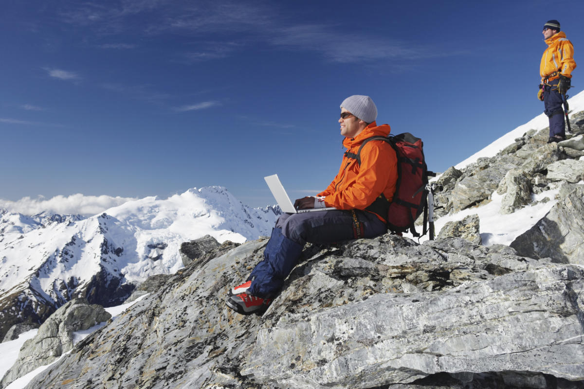 Man of mountain peak using wireless laptop in remote area