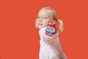 girl with pigtails against orange background holding out vote election pin