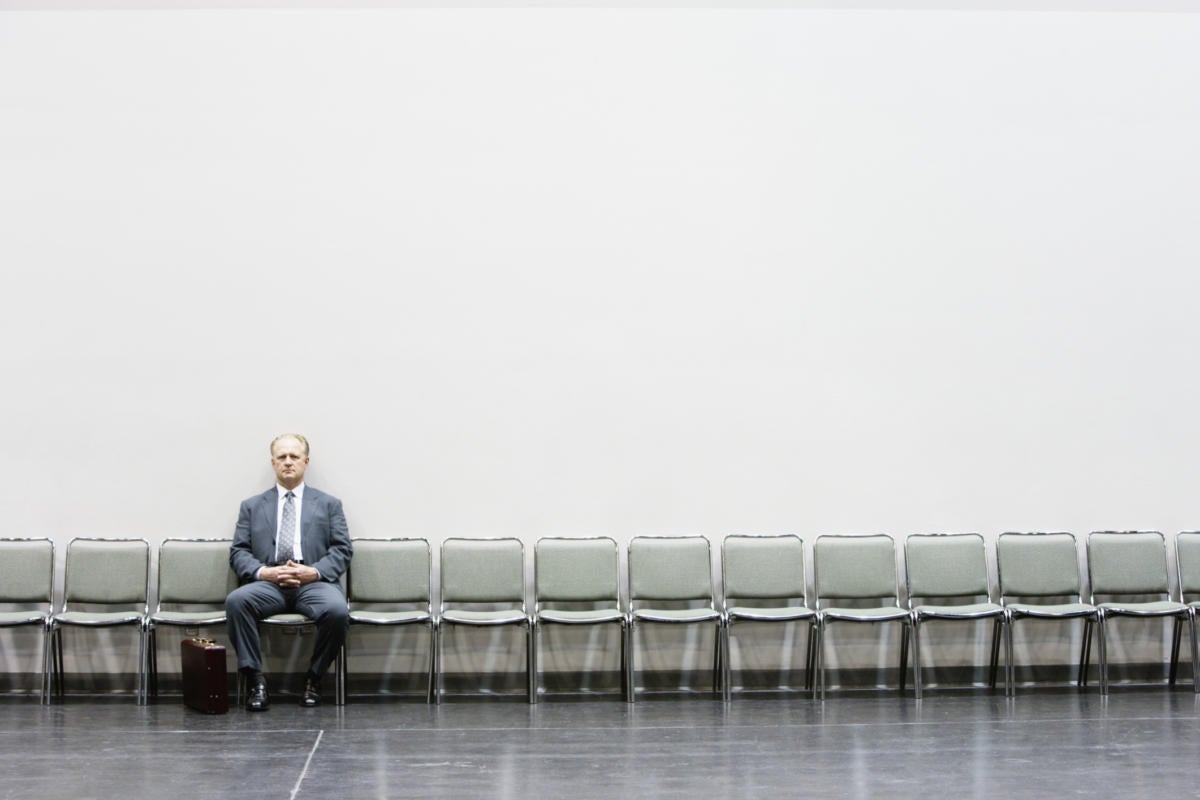 Man in blue suit waiting for interview on long row of empty chairs against white wall