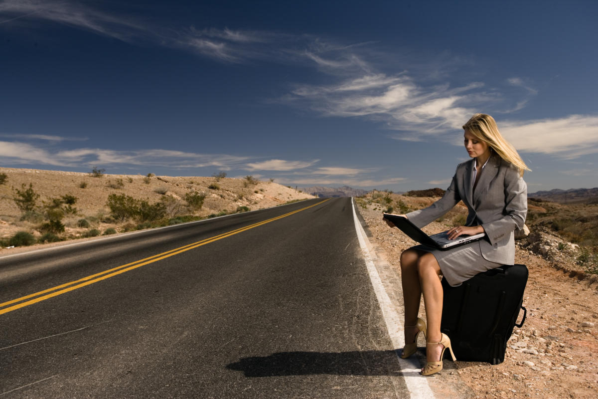 Woman on wireless laptop working on remote highway in the desert