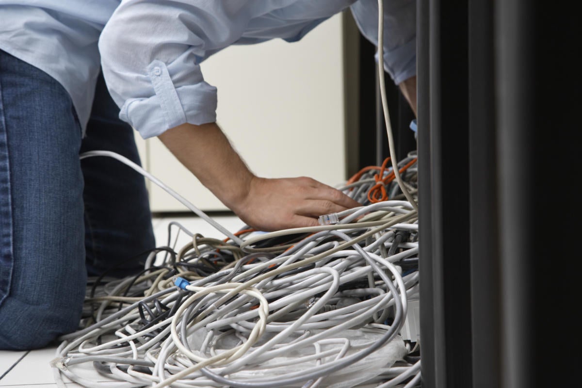 tech guy untangling network cables under desk