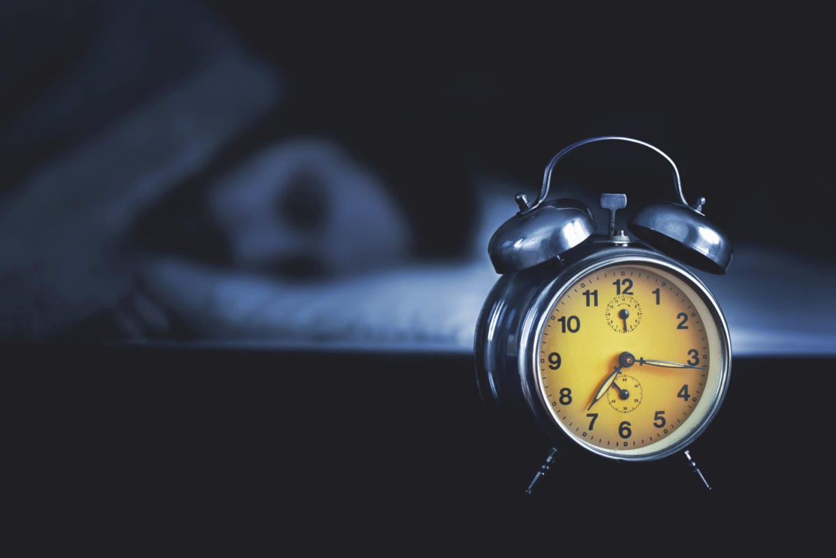 woman sleeping with yellow alarm clock in dark room