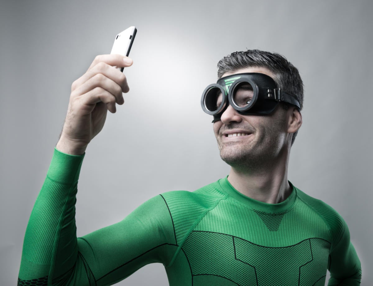 man in green superhero outfit wearing goggles taking selfie on smart phone