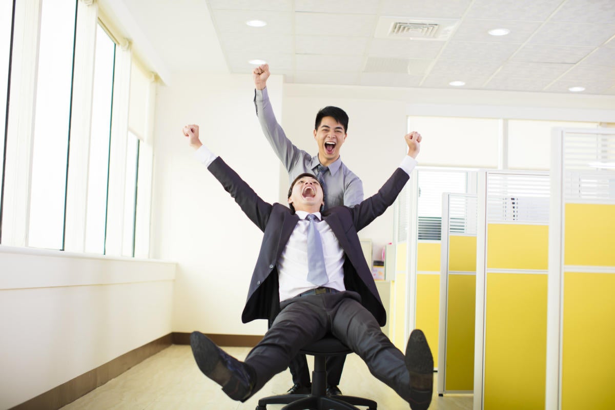 two young workers riding on office chair through office