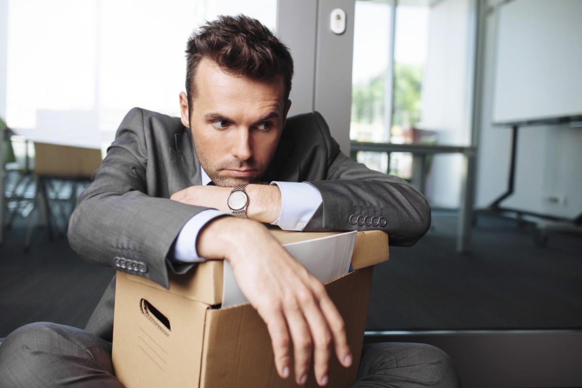 man leaning on box of office belongings after being fired or laid off