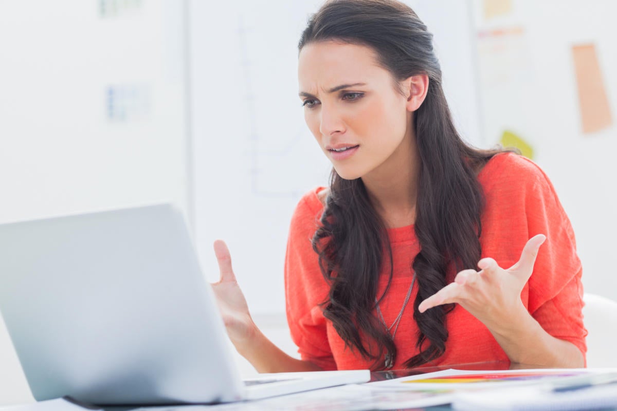 women in red shirt looking frustrated at laptop