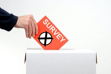 A mans hand and arm are seen depositing a survey into a sealed ballot box