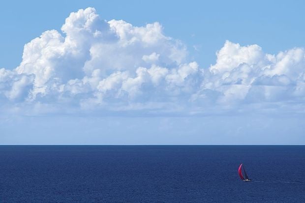 yacht with red spinnaker at full sail on blue ocean with clouds