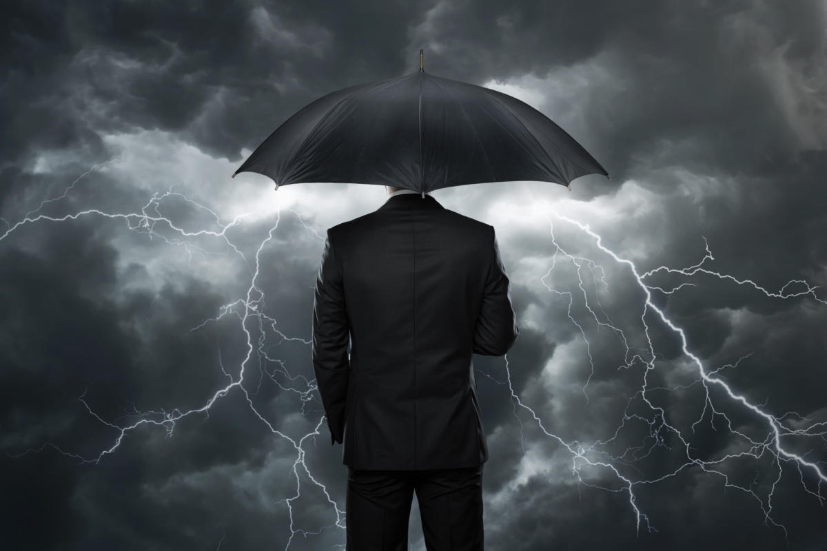 Man in black suit from behind holding umbrella with stormy skies