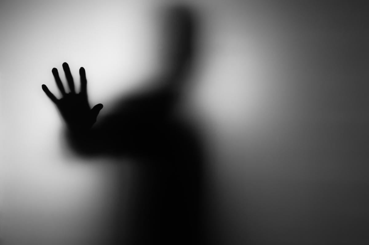shadowy figure reaching out from behind transparent wall