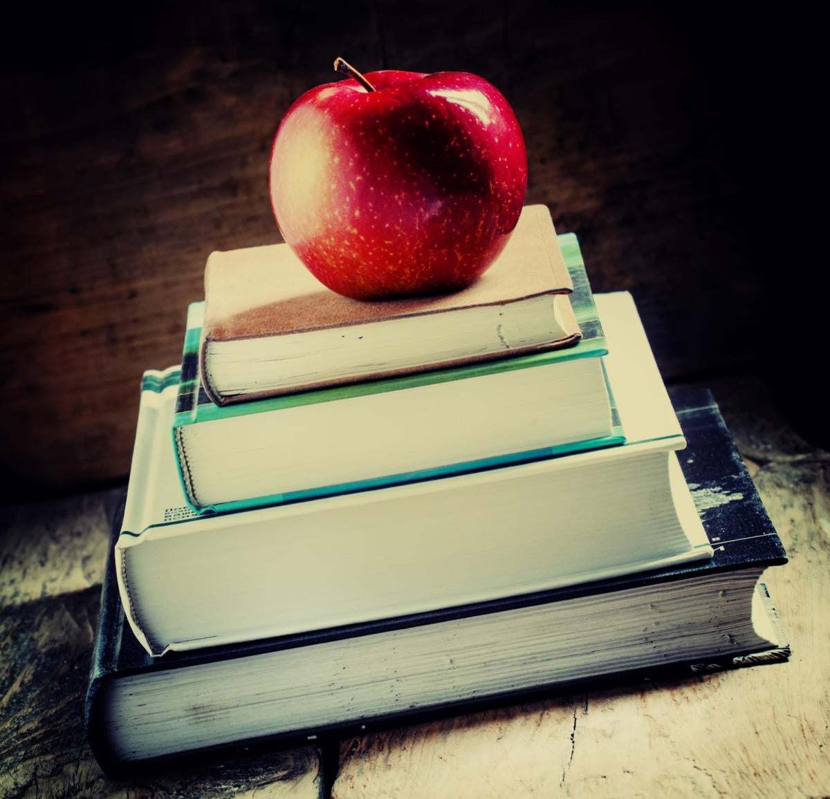 Stack of school books on desk with an apple on top